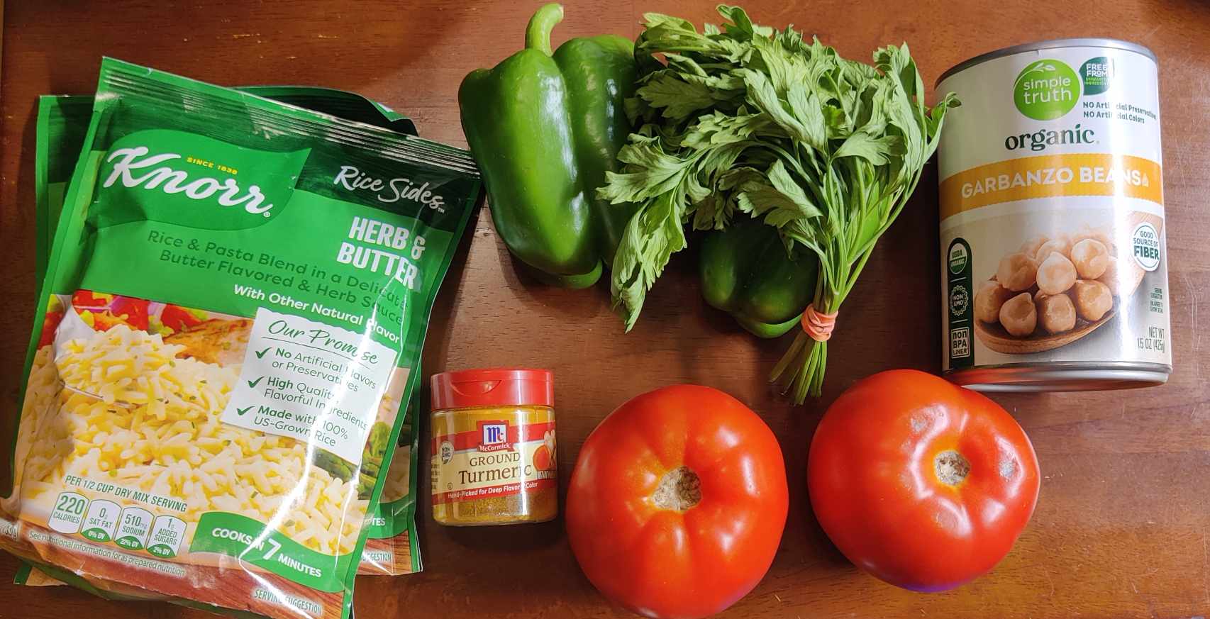 The ingredients for my loaded rice: two packets of Knorr herb and butter rice sides, two green bell peppers, two big tomatoes, some turmeric, a sprig of parsley, and a can of chickpeas (garbanzo beans)